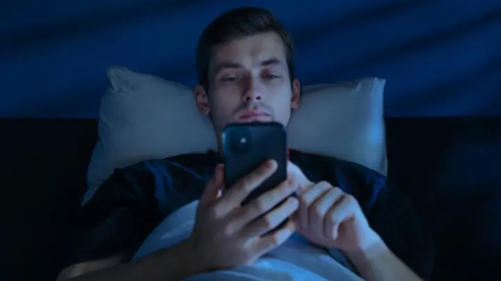 Man scrolling on his phone in bed late at night unable to sleep