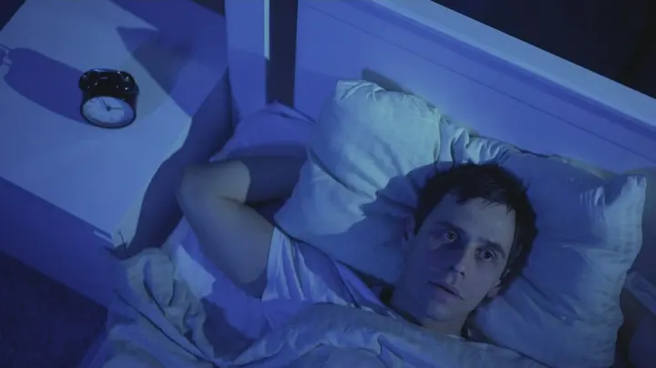 Man lying awake in bed at night staring at the ceiling unable to sleep.