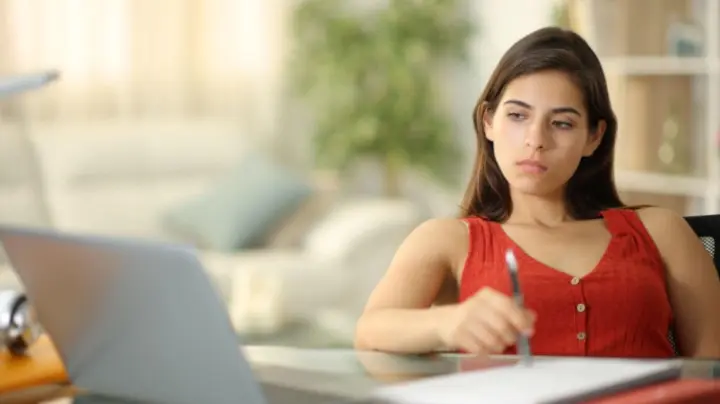 Woman sitting at a desk with a laptop looking distracted and thoughtful.
