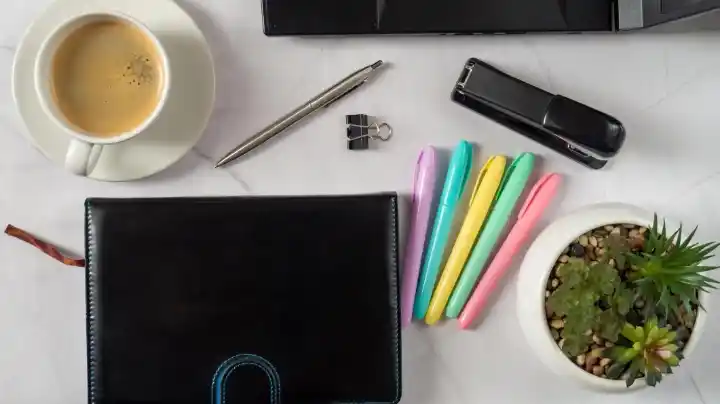 Minimal desk setup with coffee, notebook, highlighters, and office supplies arranged neatly.
