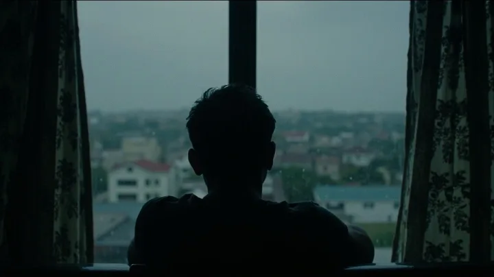 Silhouette of a man looking out the window at a city view during a quiet evening.