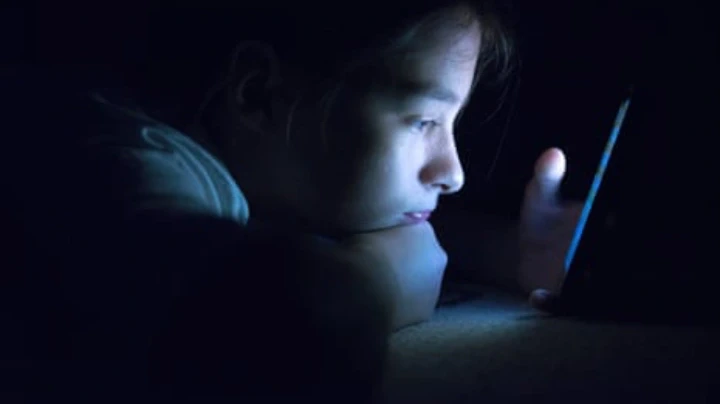 Woman lying in bed at night using her phone in the dark.