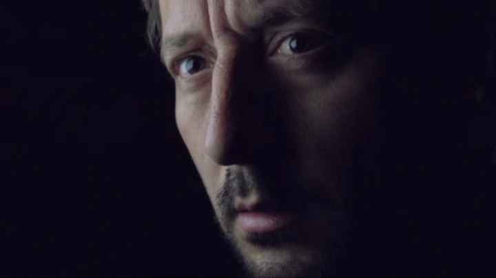 Man’s face partially lit in dark room creating a mysterious midnight thinking mood.